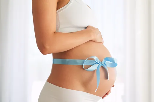 На животе беременной женщины завязан голубой бант