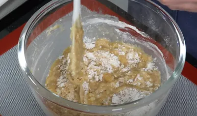 Резиновой лопаткой вмешайте смесь муки, соли и соды. Перемешивайте до тех пор, пока смесь полностью не перемешается с банановой основой. На этом же этапе нужно добавить орехи и снова перемешать. 
