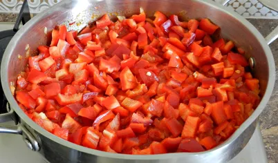 К помидорам и луку добавить нарезанный кубиками болгарский перец, перемешать, всыпать сахар, сладкую и острую паприку и тушить на медленном огне 5-7 минут.