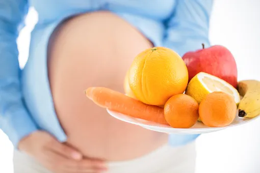 Беременная женщина держит тарелку с фруктами