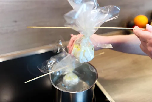 Яйца в пищевой пленке подвешивают на кастрюлю, чтобы сделать яйца пашот