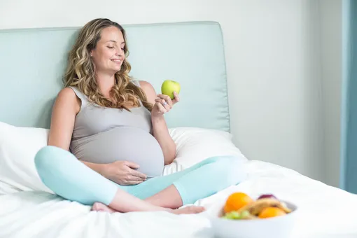 Беременная женщина держит яблоко