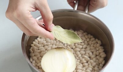 Приготовьте белую фасоль заранее. Залейте ее большим количеством холодной воды и оставьте на 8–12 часов. Затем воду слейте, налейте свежую, добавьте половину луковицы и лавровый лист, отварите фасоль до полуготовности. Отвар сохраните.