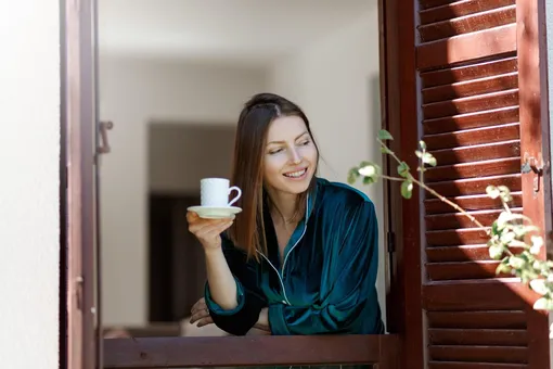 Девушка в пижаме в окне пьёт кофе