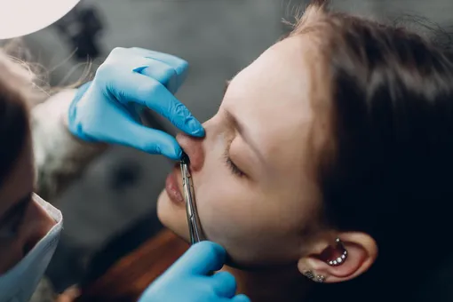 Женщине с пирсингом в ушах прокалывают нос