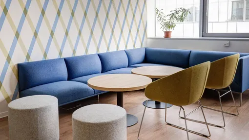 Современный интерьер со стенами и пуфиками нейтрального каменного цвета, синими диванами и круглыми столами
