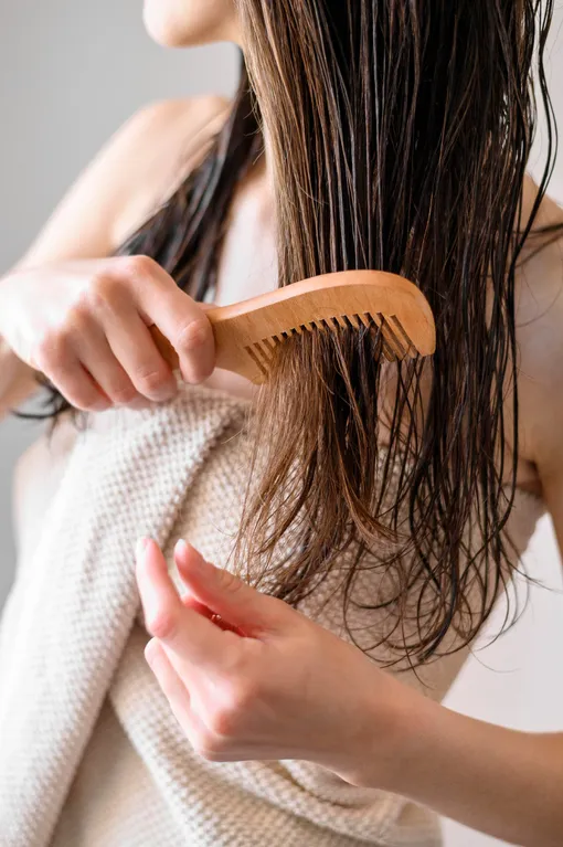 Девушка расчесывает волосы -Плюсы и минусы кокосового масла для волос, нужно ли наносить кокосовое масло на волосы и зачем