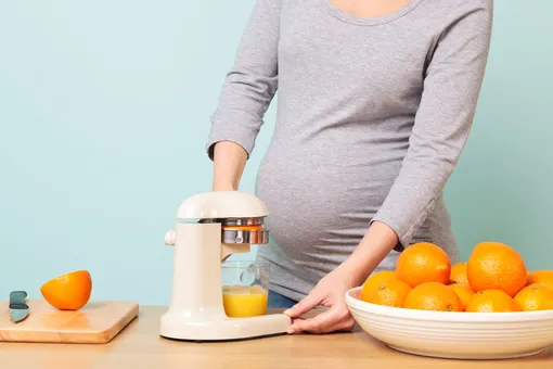 Беременная женщина делает апельсиновый сок