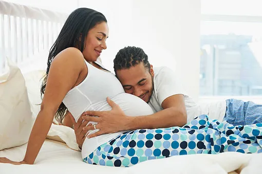 беременная женщина полулежит на кровати, мужчина рядом, обнимая и прижавшись щекой к ее животу