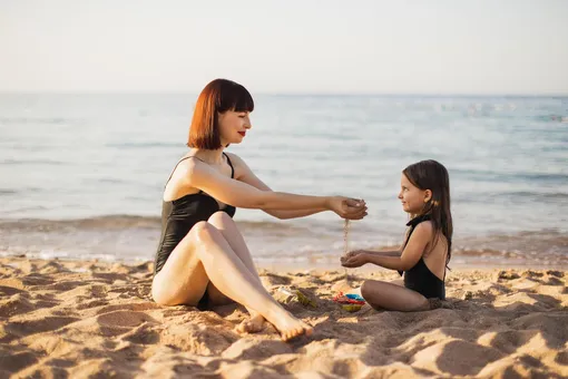 мама сыпет песок в руки дочки на пляже