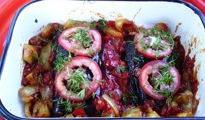 Выложите обжаренные овощи поверх фаршированных баклажанов, украсьте кружочками помидора.  Поставьте баклажаны запекаться в разогретую до 180С духовку на 15 минут. 