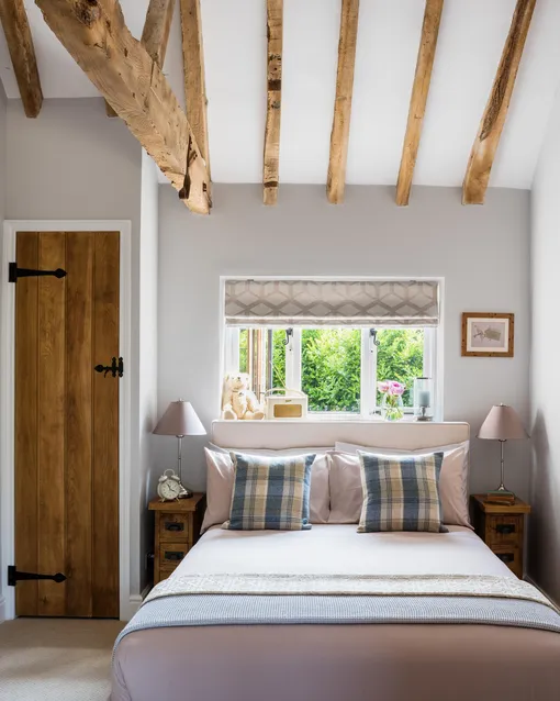 Уютная спальня с деревянными потолочными балками, узкими дощатыми прикроватными тумбочками и дверью